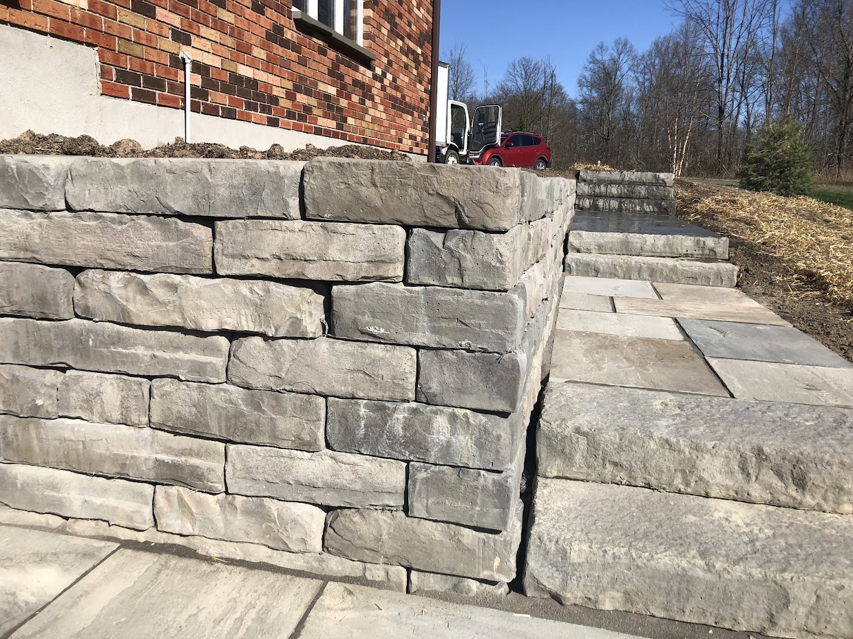 Kodah retaining wall with linear stone coursing beside a paved area and steps